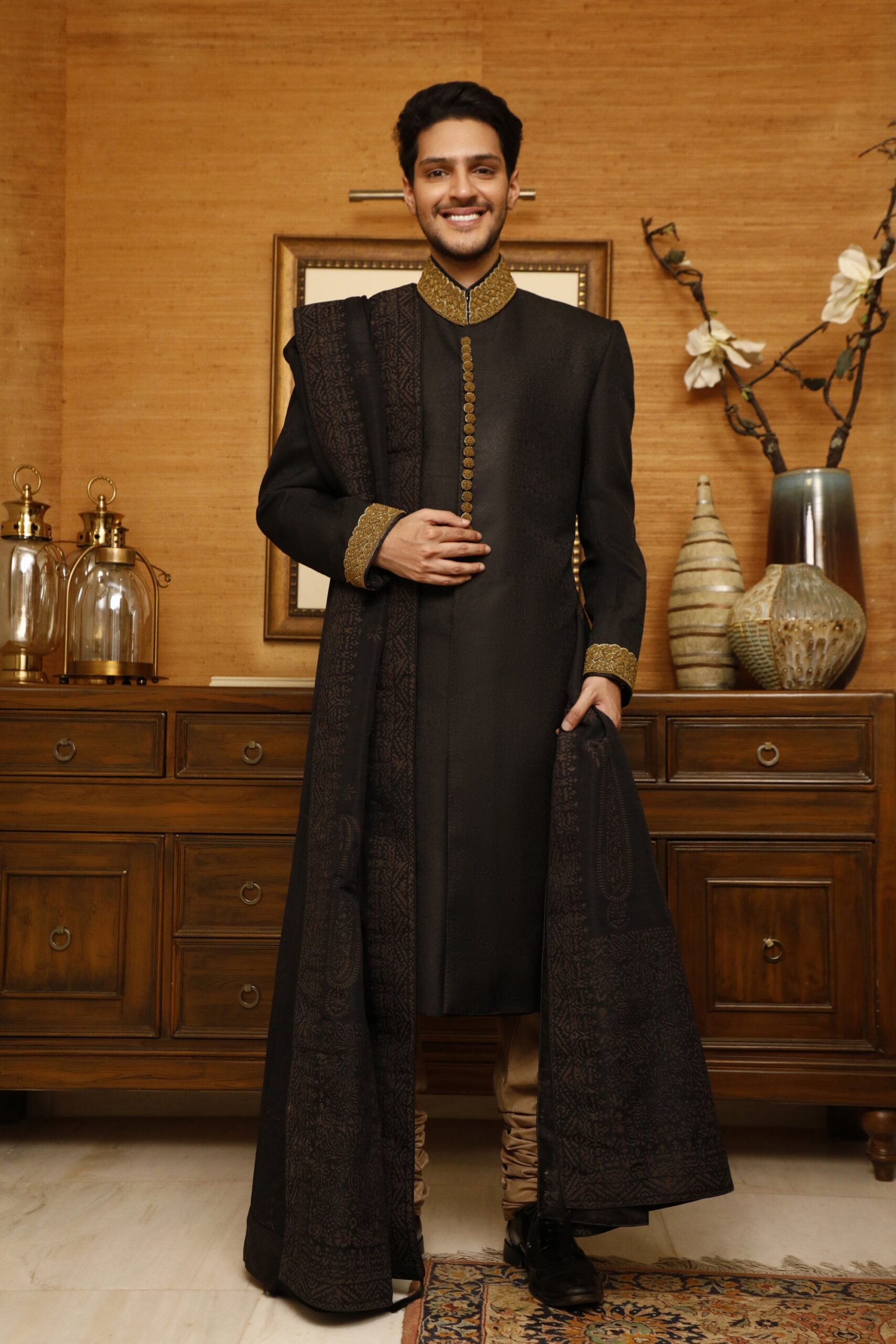 1000340352-scaled.jpg black sherwani adorned with antique gold embroidery on the collar and buttons, paired with a matching black inner suit and shawl