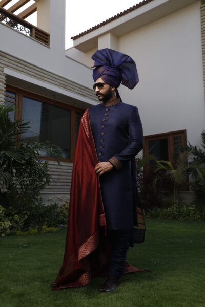 man wearing ROYAL BLUE SHERWANI for groom WITH MATCHING TURBAN PAIRED WITH A MAROON SHAWL designed by naushemian by nauman arfeen on his wedding day