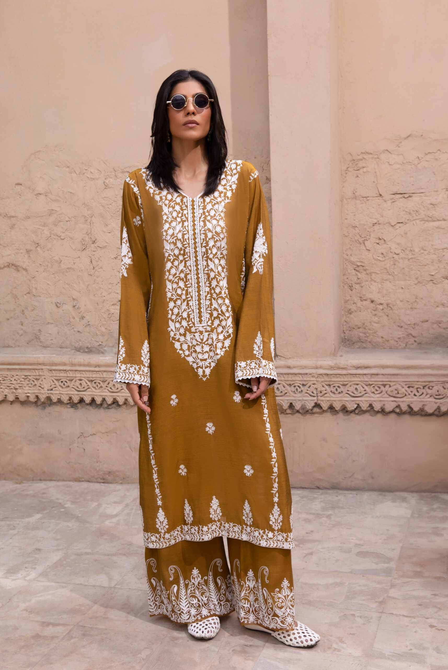 C76A6964 Rich mustard-coloured kurta Intricate white floral embroidery Elegant V-shaped embroidered neckline Full-length long kurta silhouette Embroidered sleeves and statement cuffs Scattered floral motifs on the kurta Detailed embroidered side borders Ornate embroidered kurta hem Wide-leg trousers Embroidered trouser hem Coordinated two-piece ensemble Suitable for festive and cultural occasions Elegant option for daytime and evening gatherings Contemporary silhouette with traditional detailing