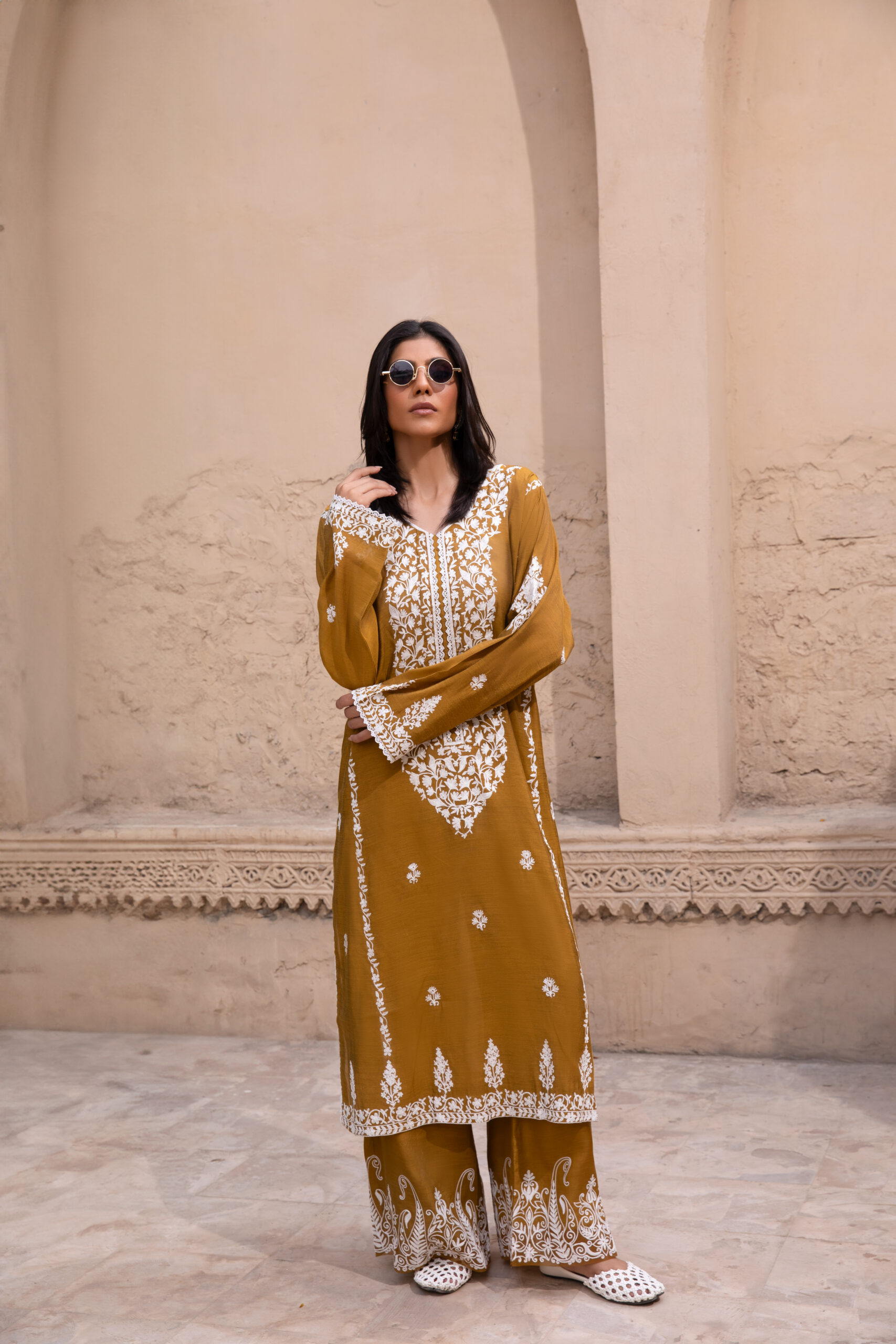 C76A6971 Rich mustard-coloured kurta Intricate white floral embroidery Elegant V-shaped embroidered neckline Full-length long kurta silhouette Embroidered sleeves and statement cuffs Scattered floral motifs on the kurta Detailed embroidered side borders Ornate embroidered kurta hem Wide-leg trousers Embroidered trouser hem Coordinated two-piece ensemble Suitable for festive and cultural occasions Elegant option for daytime and evening gatherings Contemporary silhouette with traditional detailing