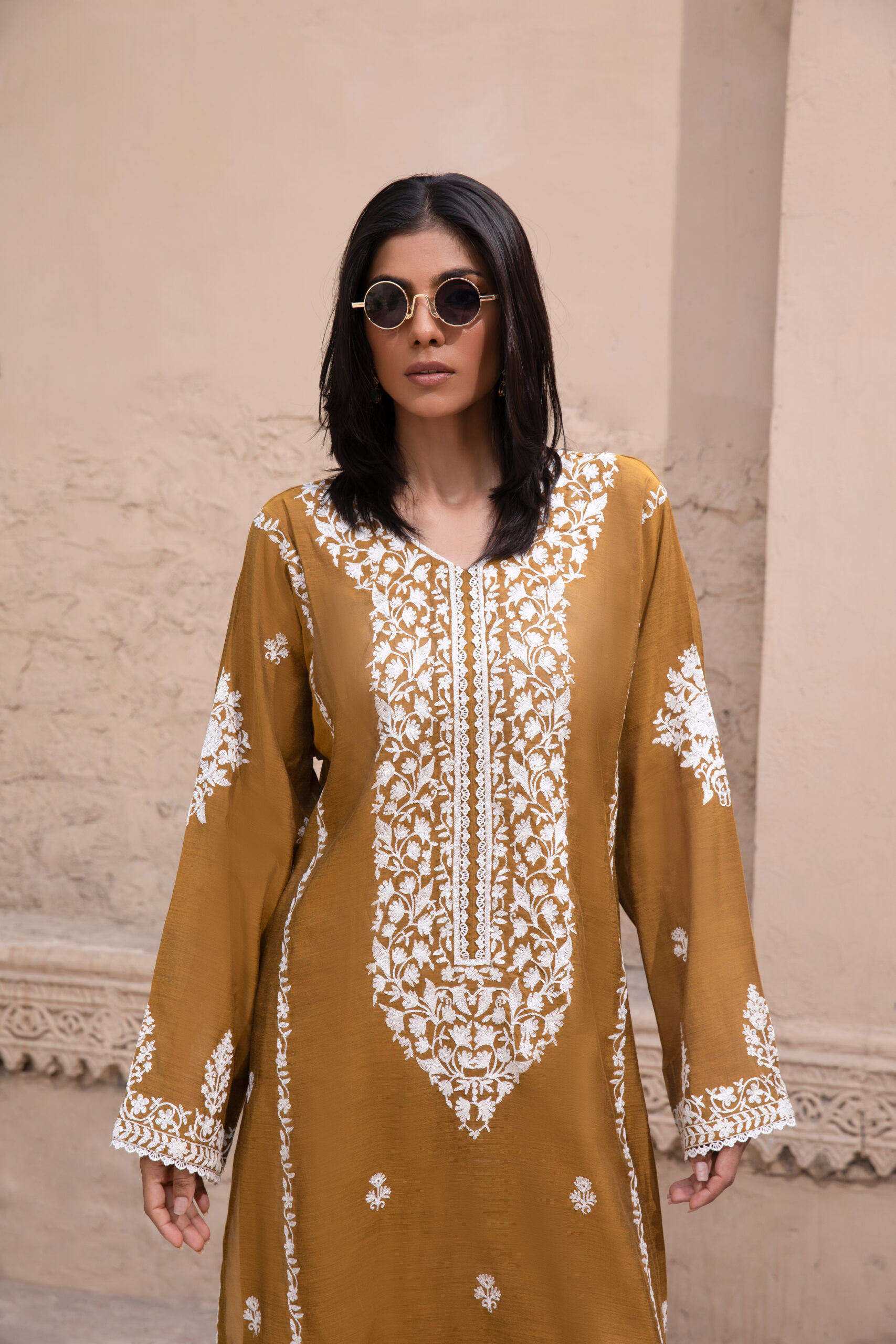 Mustard embroidered Pakistani two piece suit for women C76A6977 Rich mustard-coloured kurta Intricate white floral embroidery Elegant V-shaped embroidered neckline Full-length long kurta silhouette Embroidered sleeves and statement cuffs Scattered floral motifs on the kurta Detailed embroidered side borders Ornate embroidered kurta hem Wide-leg trousers Embroidered trouser hem Coordinated two-piece ensemble Suitable for festive and cultural occasions Elegant option for daytime and evening gatherings Contemporary silhouette with traditional detailing