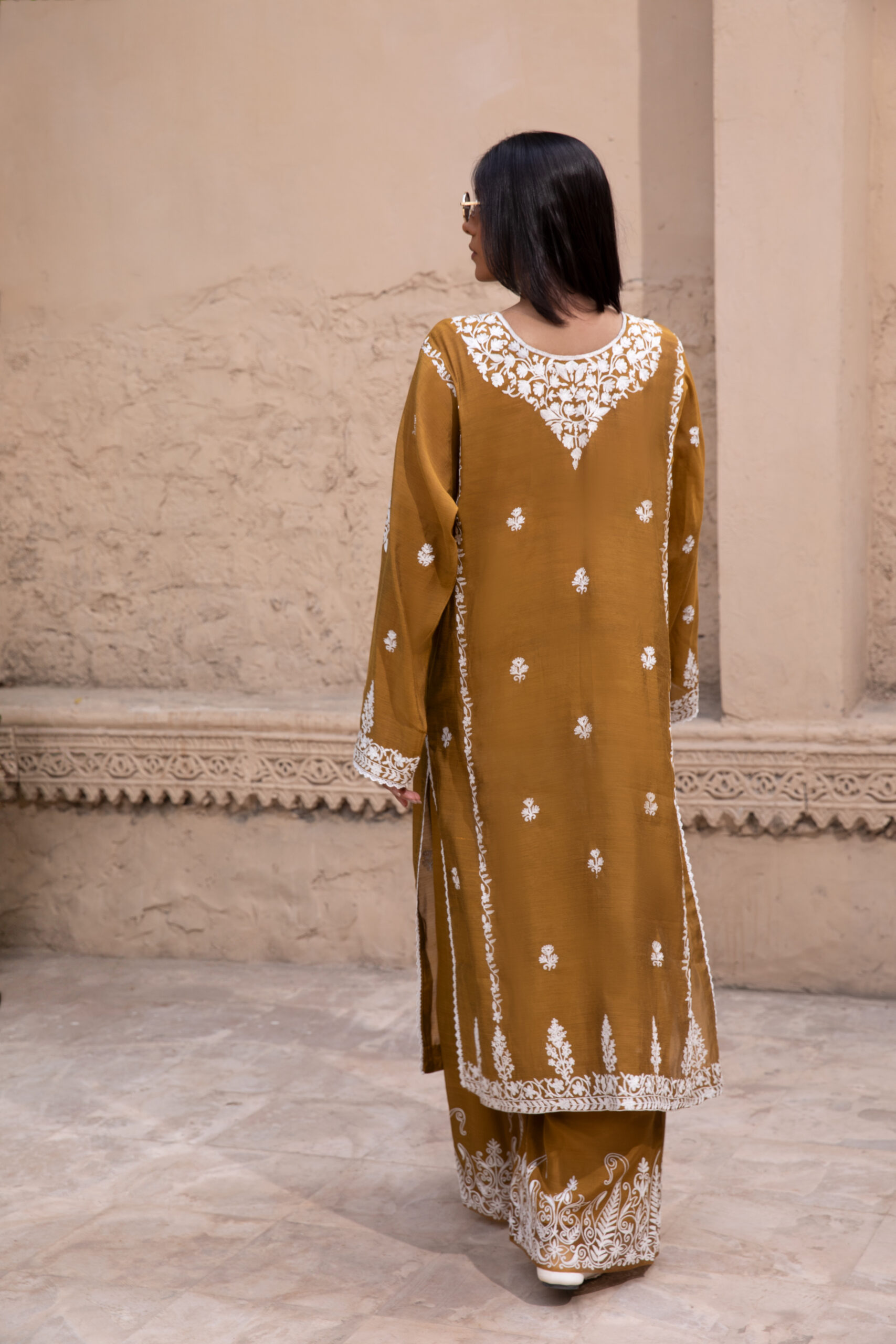 C76A6983 Rich mustard-coloured kurta Intricate white floral embroidery Elegant V-shaped embroidered neckline Full-length long kurta silhouette Embroidered sleeves and statement cuffs Scattered floral motifs on the kurta Detailed embroidered side borders Ornate embroidered kurta hem Wide-leg trousers Embroidered trouser hem Coordinated two-piece ensemble Suitable for festive and cultural occasions Elegant option for daytime and evening gatherings Contemporary silhouette with traditional detailing