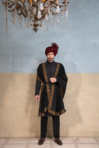 Artisan crafted black sherwani with embroidered collar and buttons, paired with black-maroon-gold shawl and maroon turban